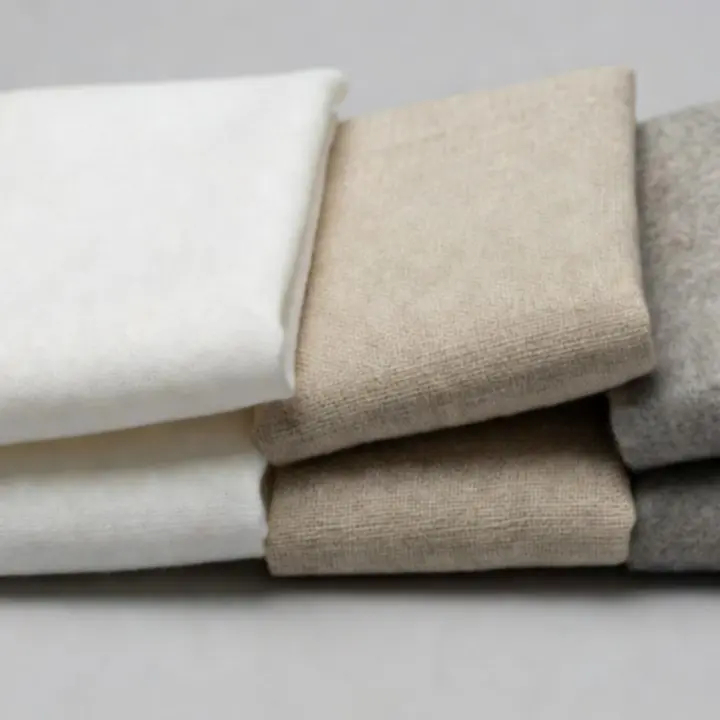 Közeli fotó párnák és takarók szövetéről, jól kivehető szövéssel és természetes színárnyalatokkal.